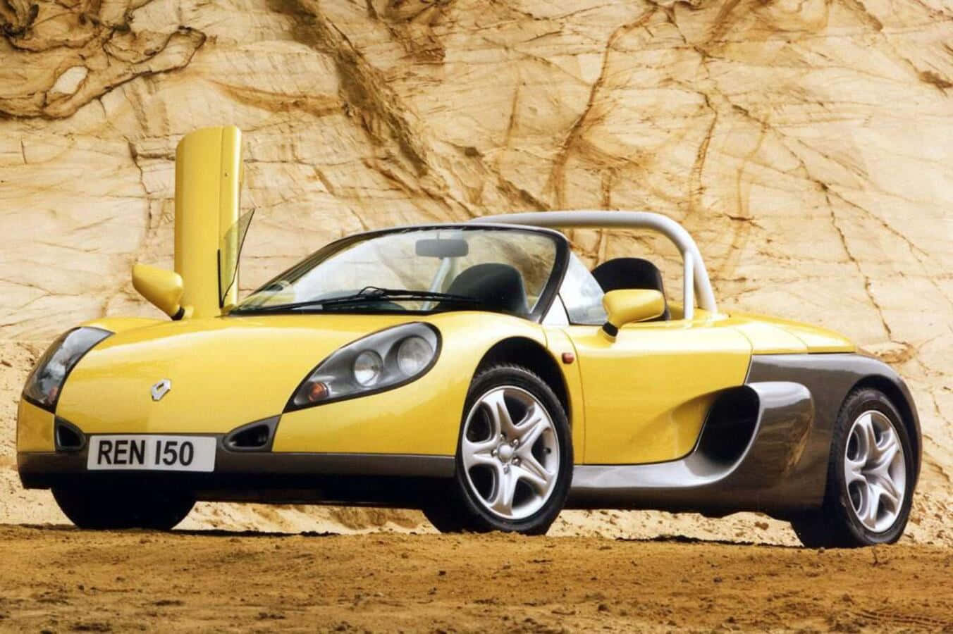 Renault Sport Spider 桌布 壁紙 — 一輛亮黃色的雷諾Spider跑車配備鷗翼車門，停靠在紋理米色岩壁前。
