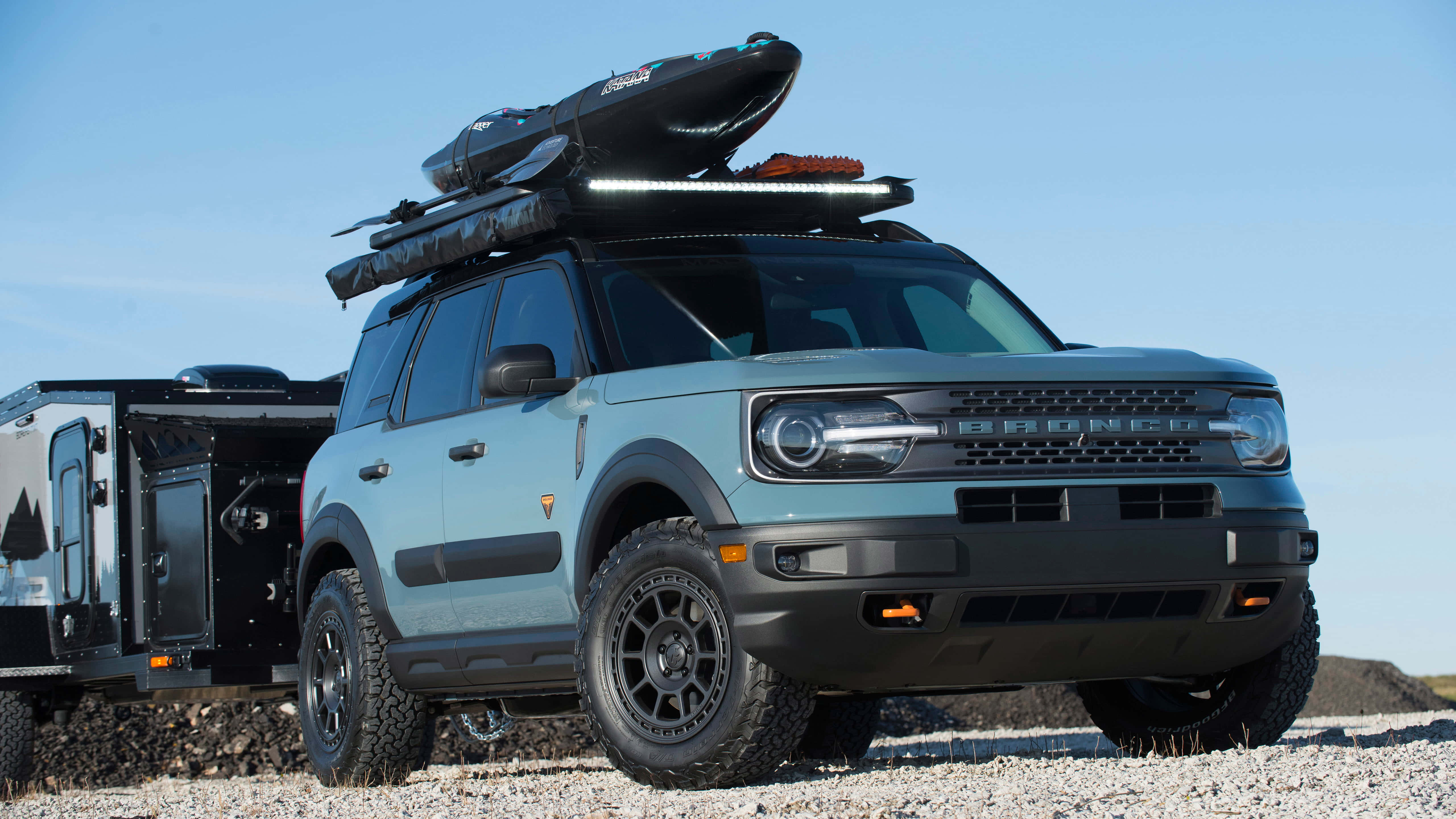 福特Bronco — 冒險即將開始 壁紙 — 一輛淺藍色的福特Bronco，車頂行李架上載著皮划艇和裝備，在晴朗藍天下的礫石平原上準備好冒險。