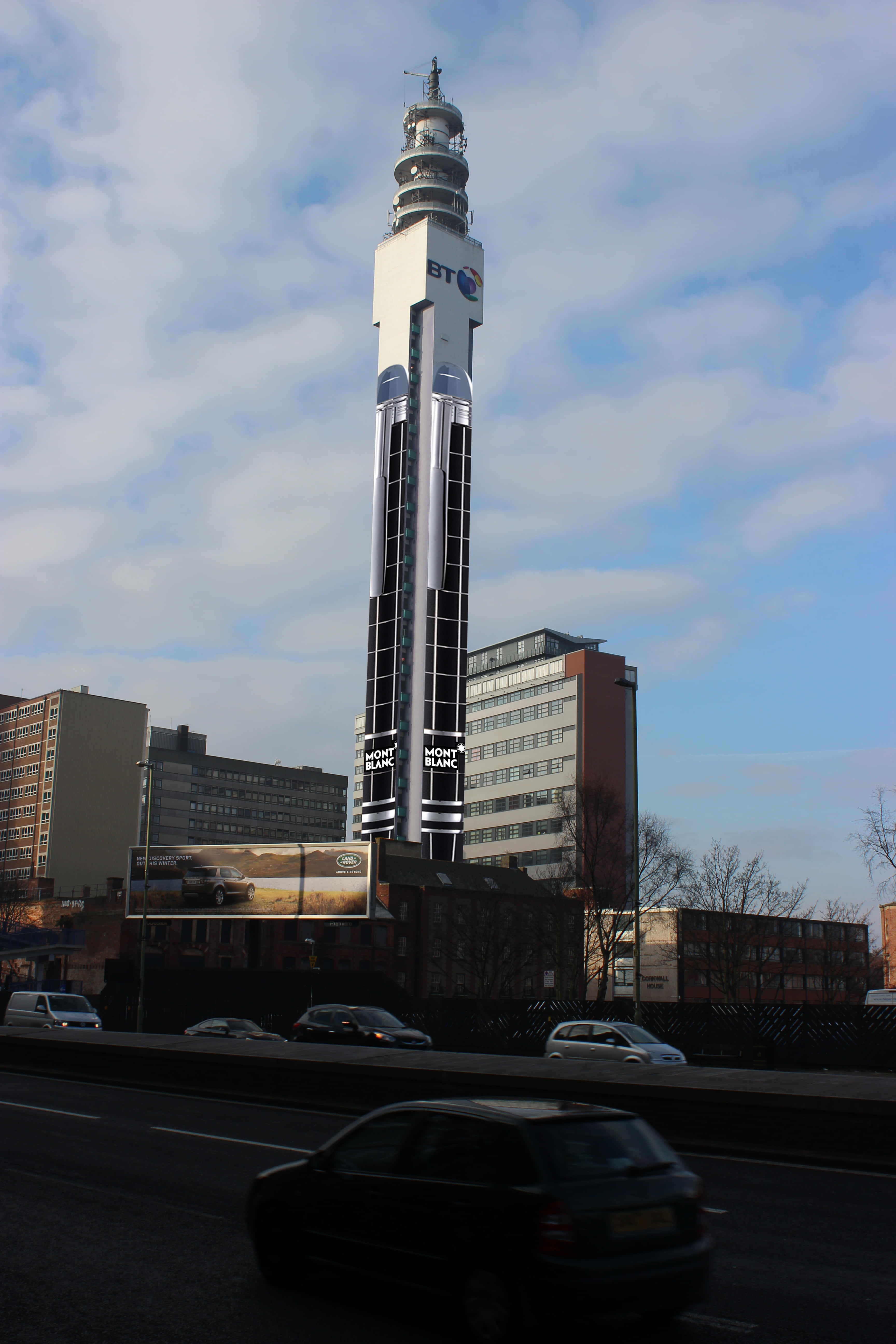 BT 塔高聳於城市之上手機壁紙 壁紙 — 一座高聳的BT建築物帶有Mont Blanc品牌標誌，聳立在部分多雲的天空下，汽車在城市的街道上行駛而過。