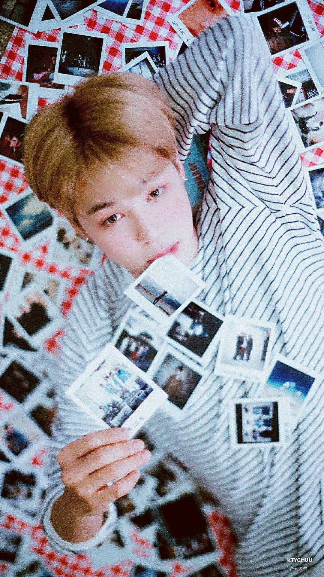 BTS 2020 吉米 壁紙 — 一個有雀斑的年輕男子穿著條紋襯衫，躺在紅色格紋表面上，周圍散落著寶麗來照片。