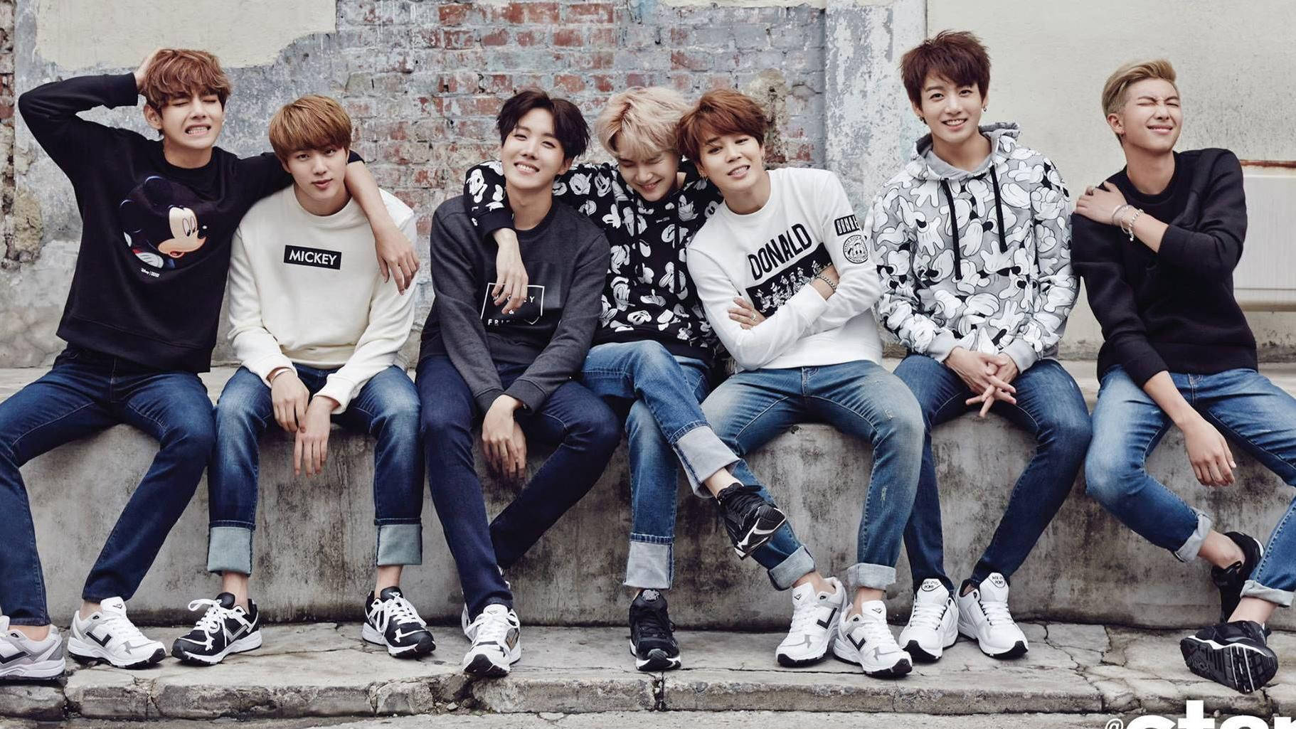 BTS 2020 坐在混凝土長凳上 壁紙 — 七個年輕男子身穿休閒街頭服飾，一起坐在風化的混凝土邊緣上，背靠磚牆，微笑著對著鏡頭擺姿勢。