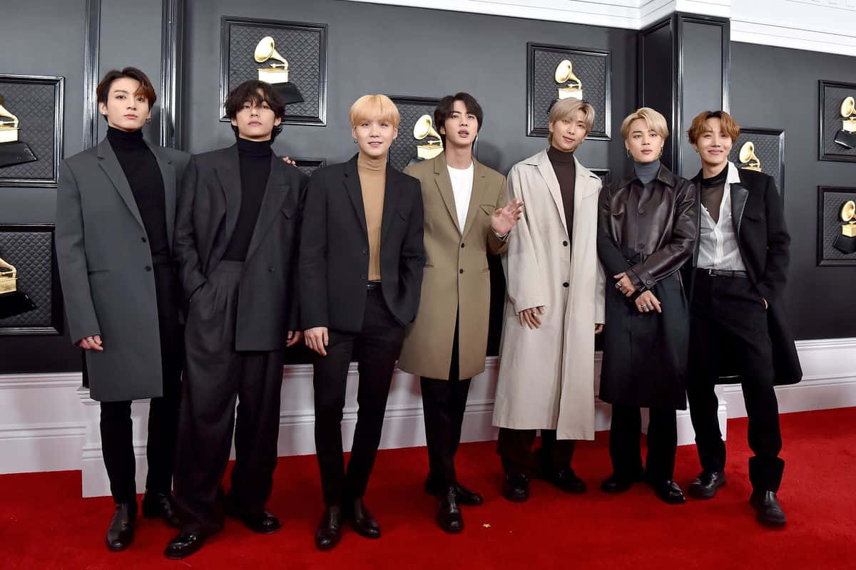 BTS 2020 格萊美紅毯照片 壁紙 — 七位時尚男士穿著別緻大衣，在葛萊美獎背景下自信地擺姿勢於紅地毯上。