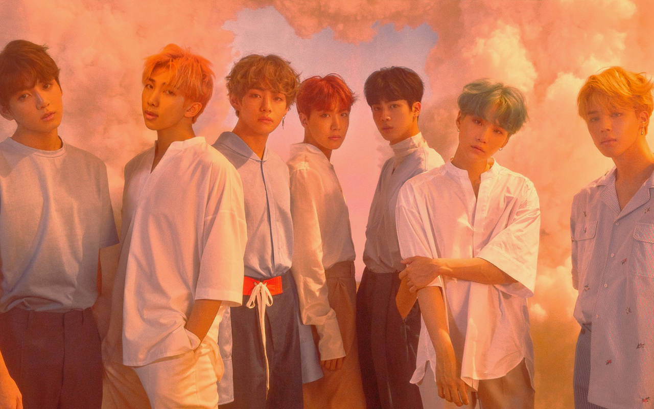 BTS 2020 淡雅濾鏡 壁紙 — 七個頭髮色彩繽紛的年輕男子排成一排，背景是夢幻的粉紅和橙色雲朵，穿著寬鬆的白襯衫。