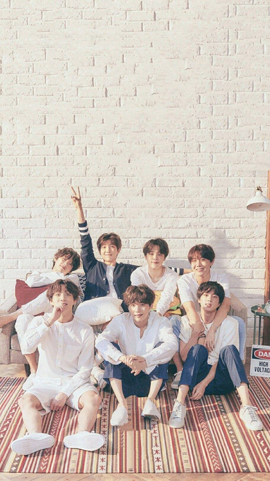 BTS 2020 美學集體照 壁紙 — 七位身穿白色休閒裝的年輕男子在圖案地毯上，以白色磚牆為背景，愉快地擺姿勢。