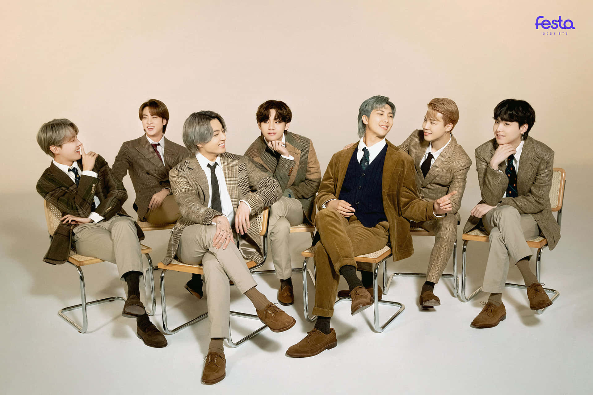 BTS 2021 Festa 棕色主題照片 壁紙 — 七位時尚年輕男士身穿協調的棕色西裝，隨意地坐在木椅上，背景是柔和的米色工作室背景。