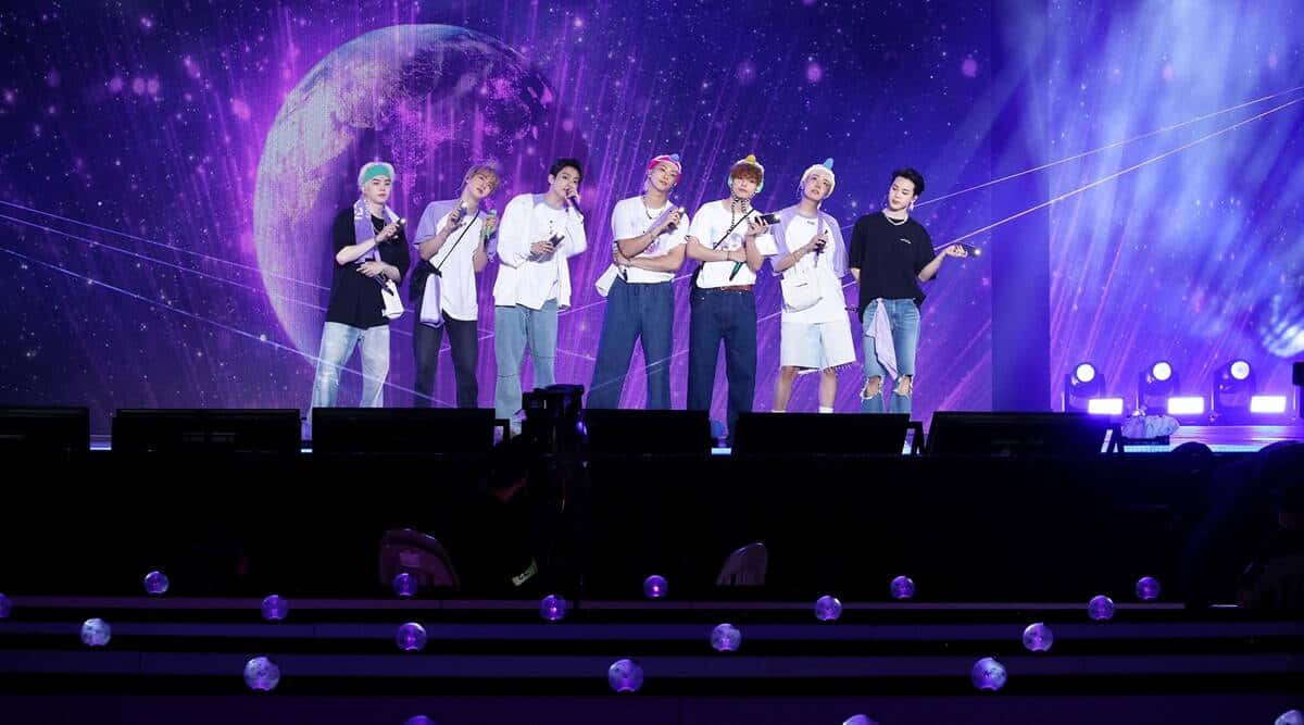 BTS 2021 Muster Sowoozoo 演出照片 壁紙 — 七位表演者身穿休閒服裝，站在沐浴在紫色燈光下的舞台上，背景是宇宙，有一個發光的星球。