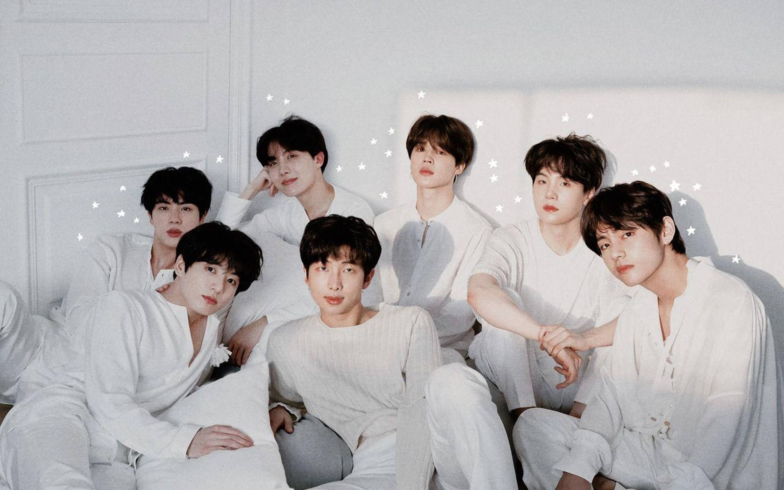 BTS 2021 Tear U時代桌面壁紙 壁紙 — 七個穿著白色休閒服的年輕男子在床上一起擺姿勢，背景是帶有星星貼紙的白色鑲板牆。