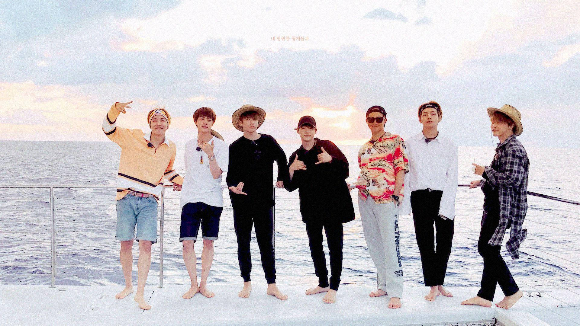 BTS 2021 桌面壁紙《Bon Voyage》 壁紙 — 七名男子穿著休閒夏季服裝，在日落時分赤腳站在船甲板上，身後是平靜的海洋。
