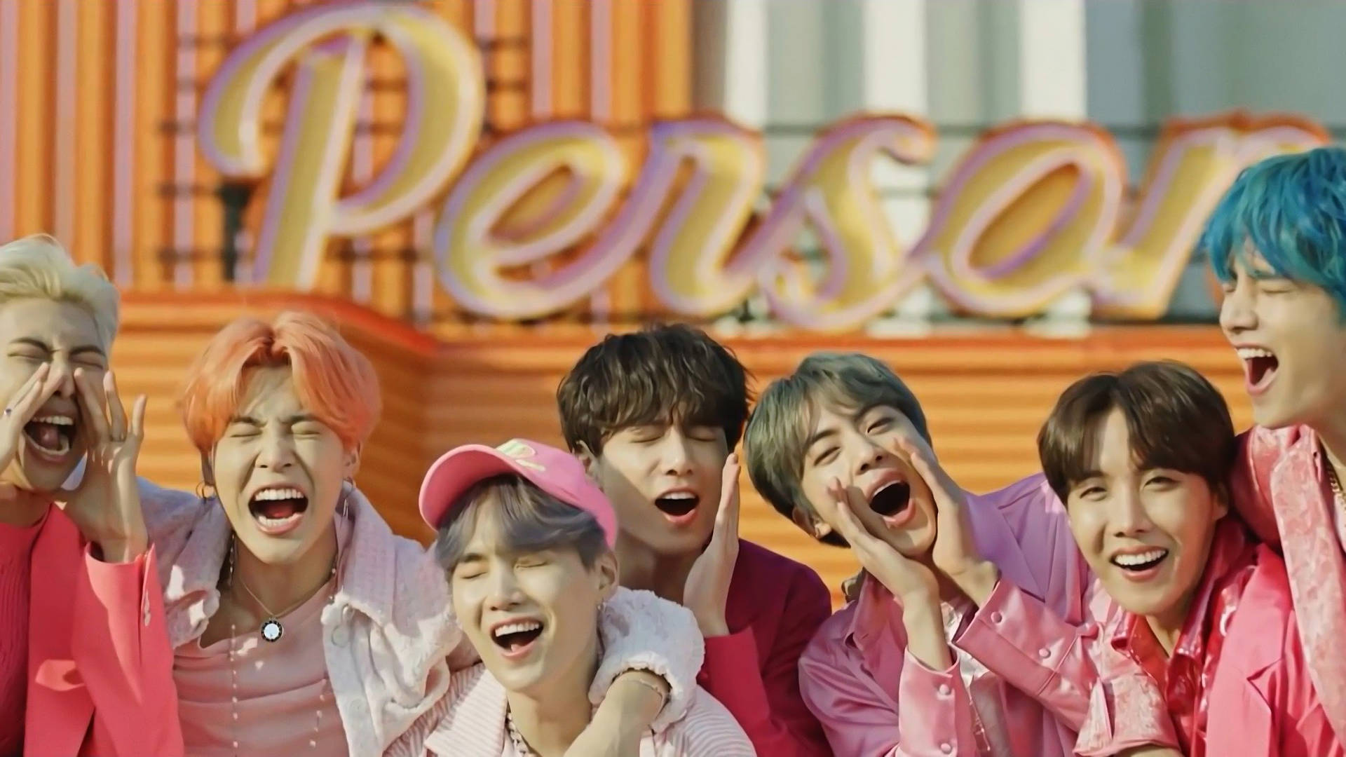 BTS 2021 桌面壁紙《Boy With Luv》 壁紙 — 七位擁有繽紛髮色的年輕男性在一個寫著「Person」的大型粉紅色霓虹燈牌前開懷大笑。