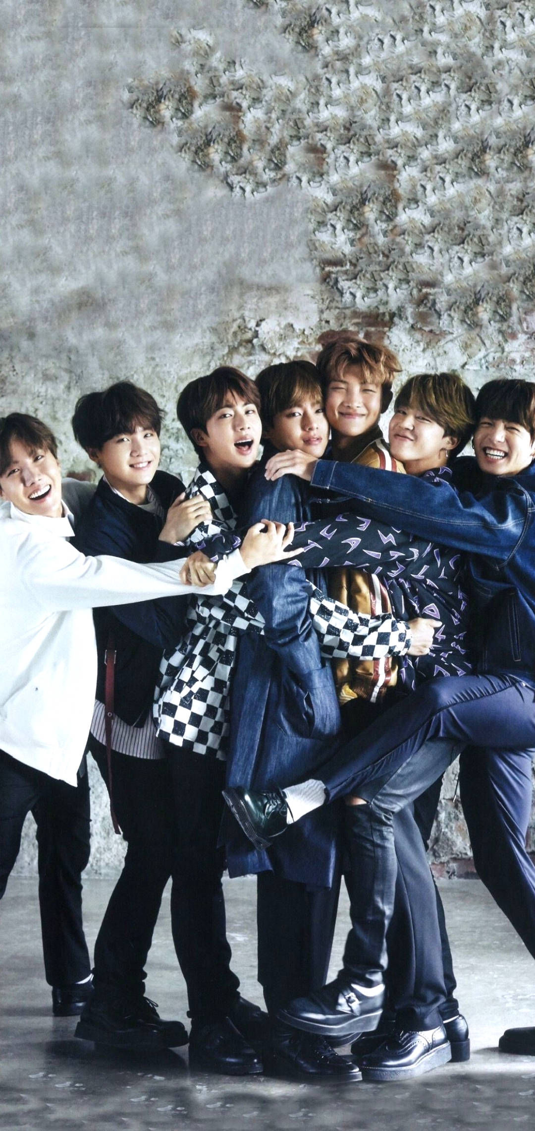 親密 BTS 鎖屏 壁紙 — 七位微笑的年輕男子穿著休閒服裝，擠在一起靠著紋理混凝土牆，擺出歡樂的團體姿勢。