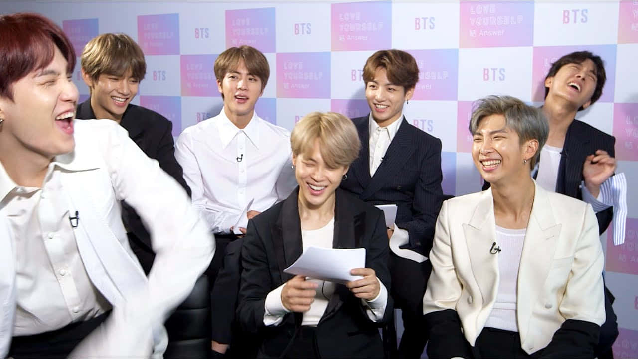 BTS - BTS - BTS - BTS - BTS - B 壁紙 — 七個微笑的男人穿著西裝，在粉紅色和白色的BTS品牌背景前笑著擺姿勢。