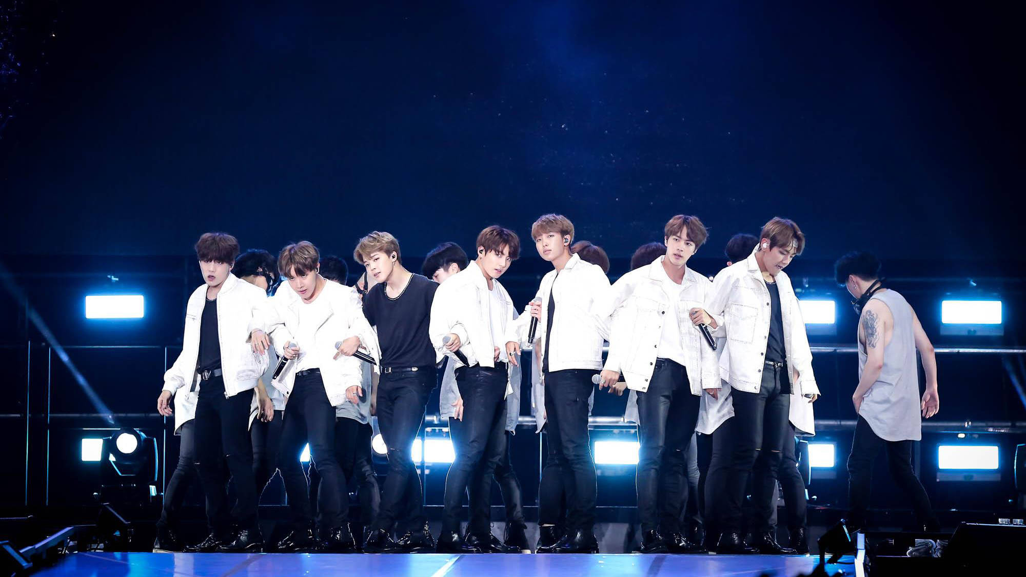 世界巡迴酷炫BTS筆電壁紙 壁紙 — 一個K-pop組合在黑暗舞台上充滿活力地表演，舞台被明亮的藍色聚光燈和煙霧效果照亮。