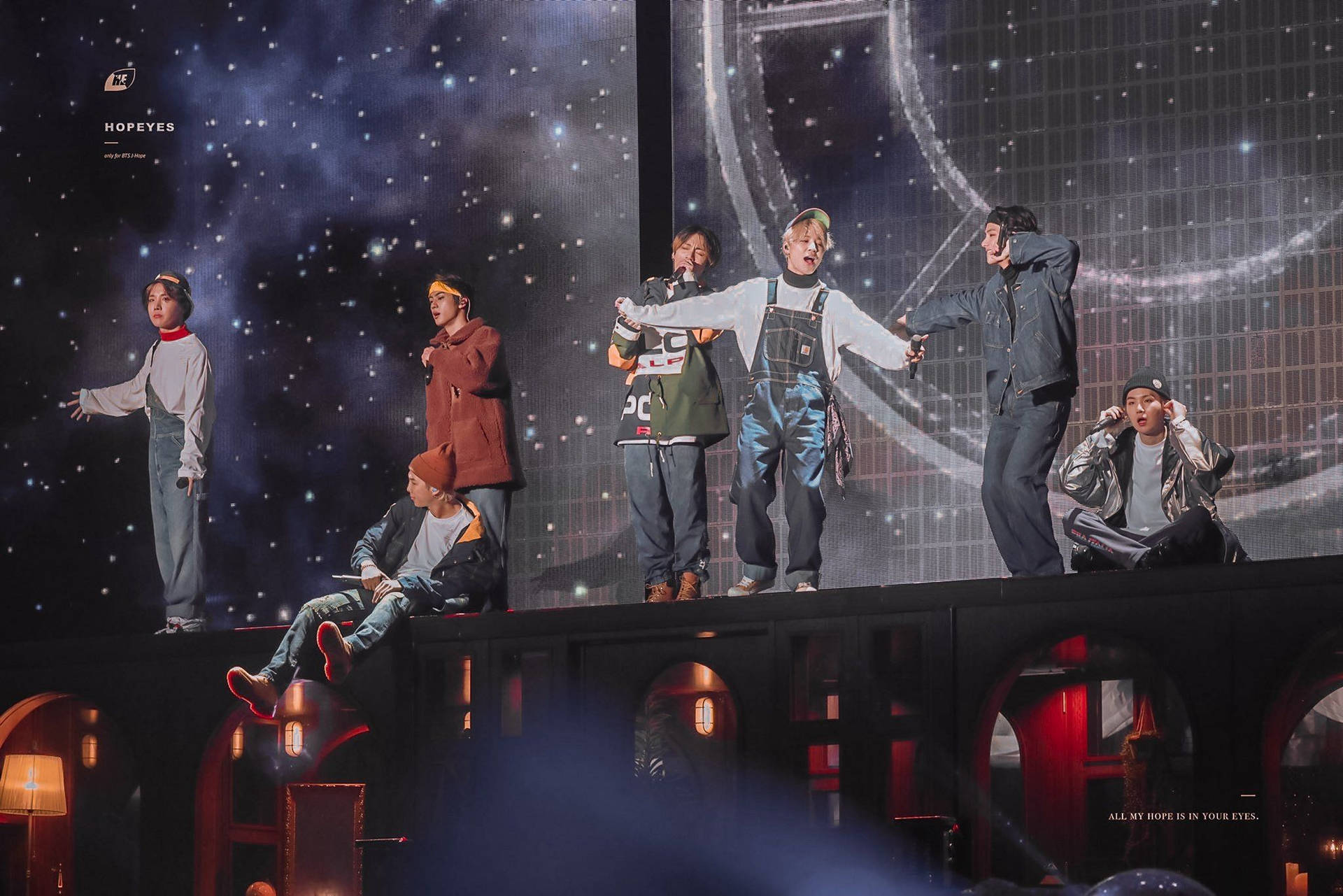 BTS《GoGo》表演舞台 壁紙 — 七位表演者在一個帶有星空宇宙背景和下方發光拱門的舞台上擺出動態姿勢。