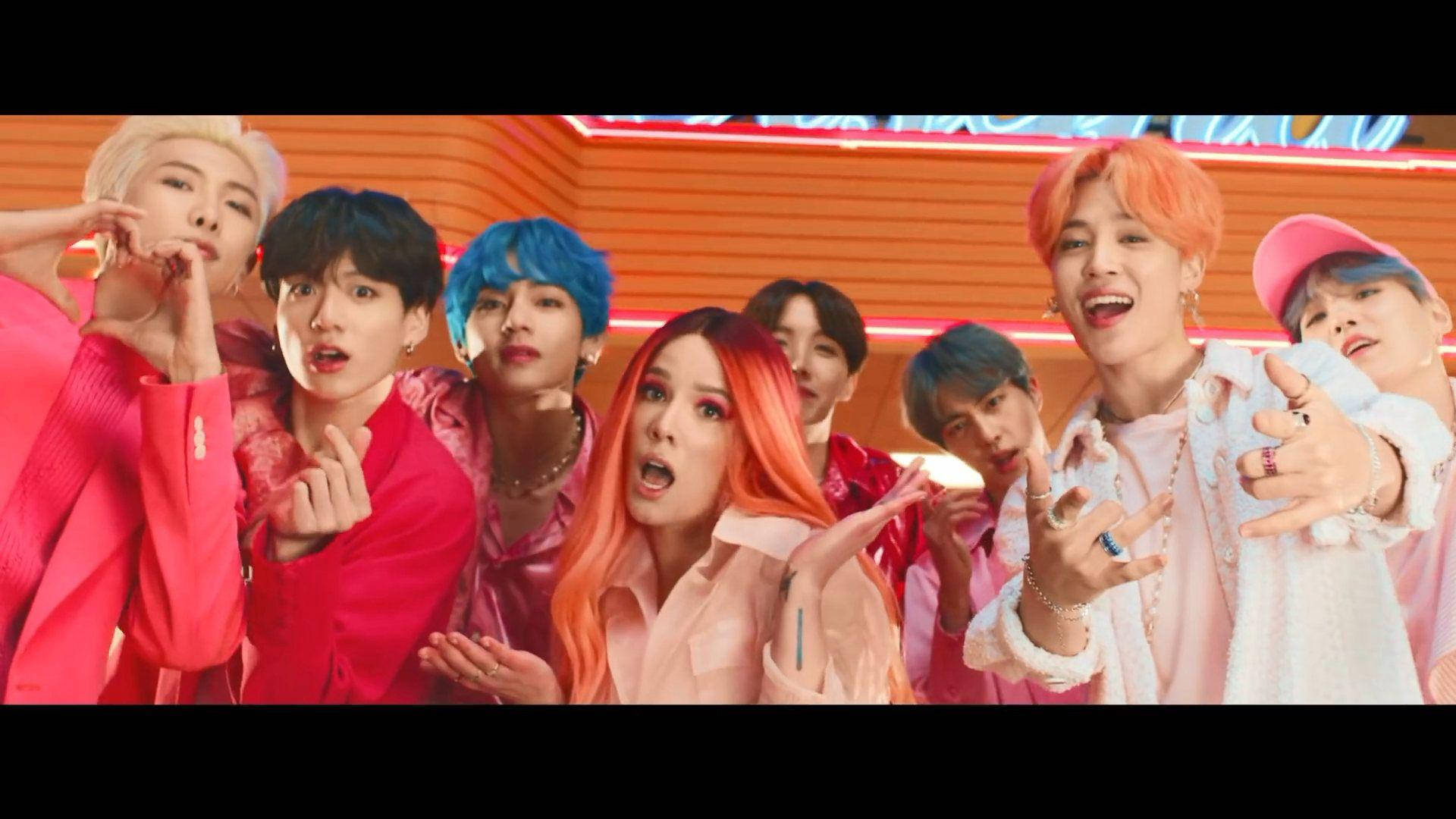 BTS 與 Halsey《Boy With Luv》MV 桌面壁紙 壁紙 — 一群充滿活力的K-pop偶像，擁有色彩繽紛的頭髮和大膽的服裝，在發光的橙色霓虹燈背景下充滿活力地擺姿勢。