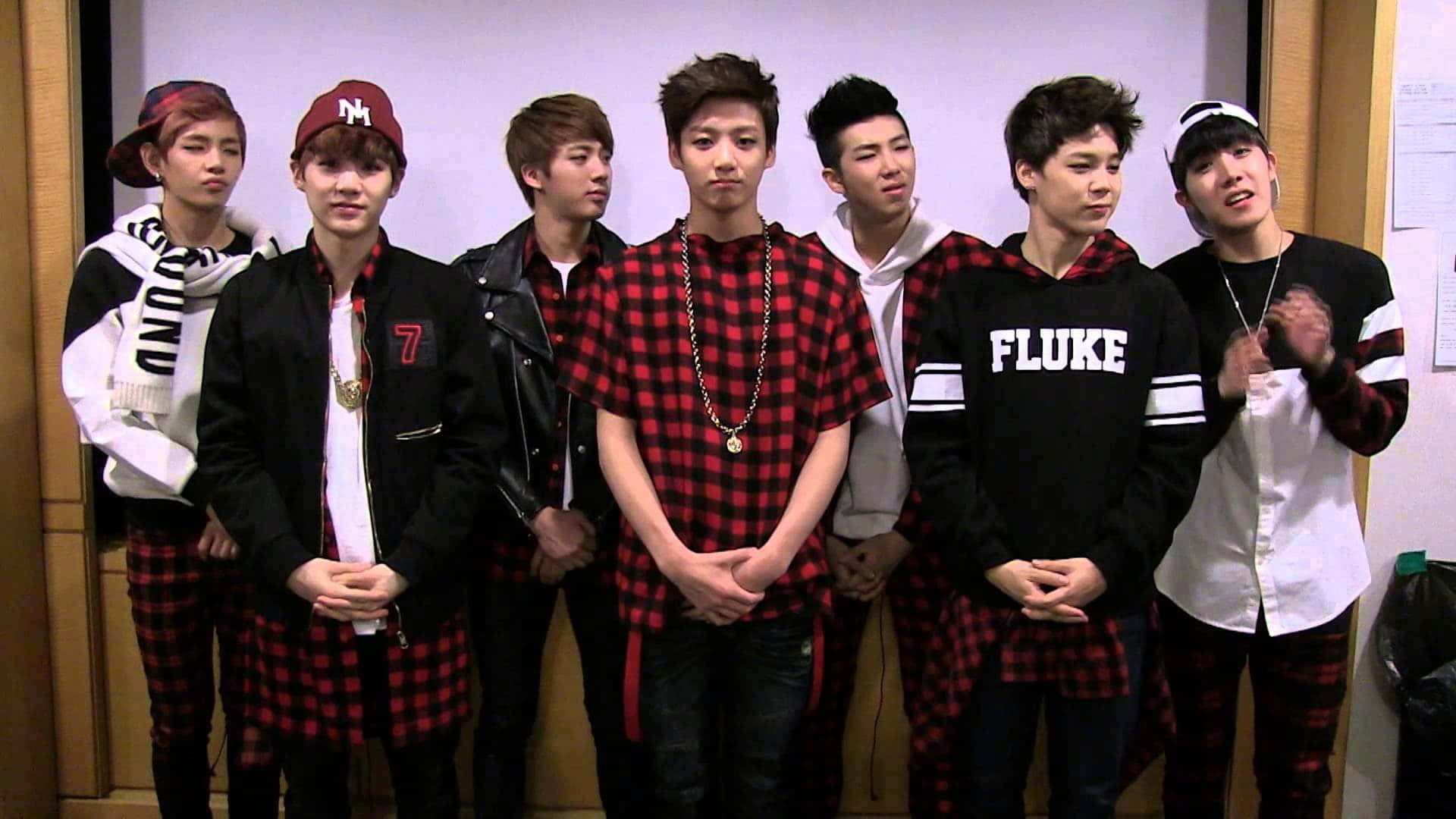 七位身穿相配紅色格仔服飾的年輕男性K-pop偶像正在拍照。