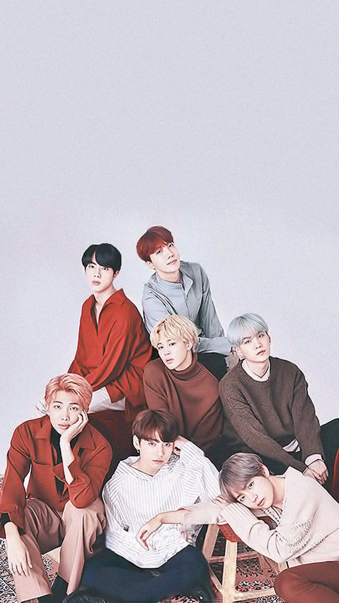 BTS iPhone 背景 壁紙 — 七位時尚年輕男士身穿大地色系，在淺灰色背景前隨意擺姿勢，帶有柔和陰影。