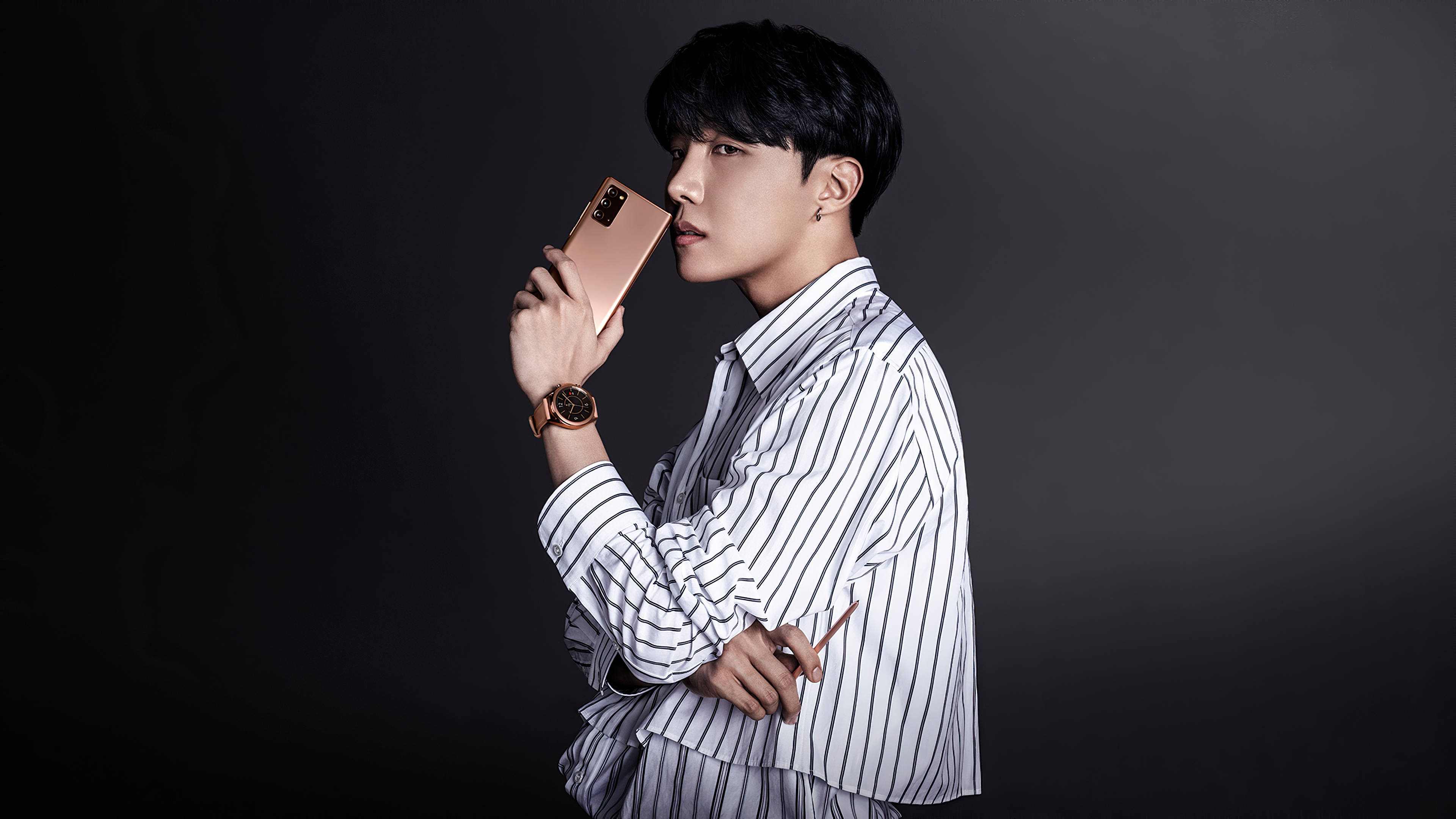 BTS J-Hope 手機模特兒美學照 壁紙 — 一位穿著條紋襯衫的時尚男士在深色漸變背景前拿著玫瑰金色手機。