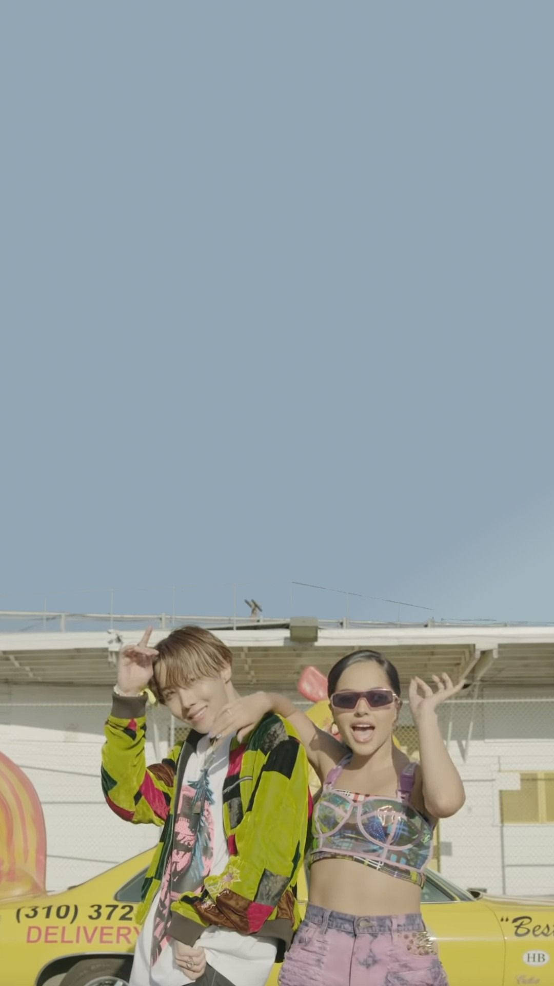 BTS J-hope 與 Becky G 壁紙 — 兩位時尚年輕人在晴朗藍天下，俏皮地在一輛黃色送貨車旁擺姿勢。