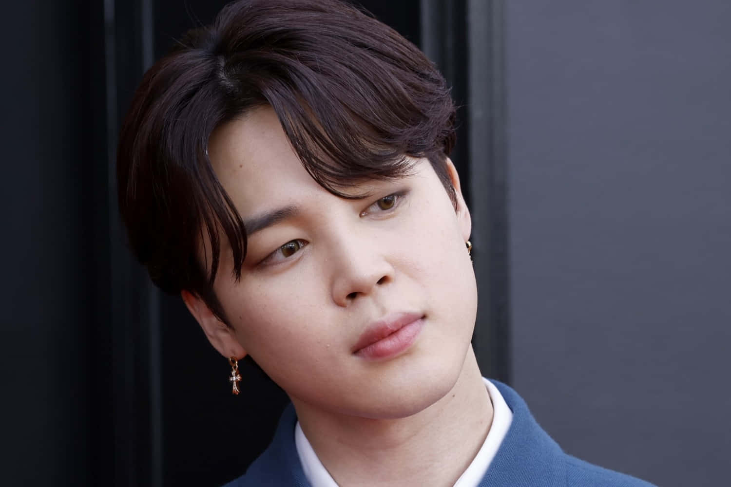 BTS Jimin 出席 2021 格萊美獎 壁紙 — 特寫肖像，一名黑髮、戴金耳環的年輕男子，身穿藍色西裝外套，背景為深色。