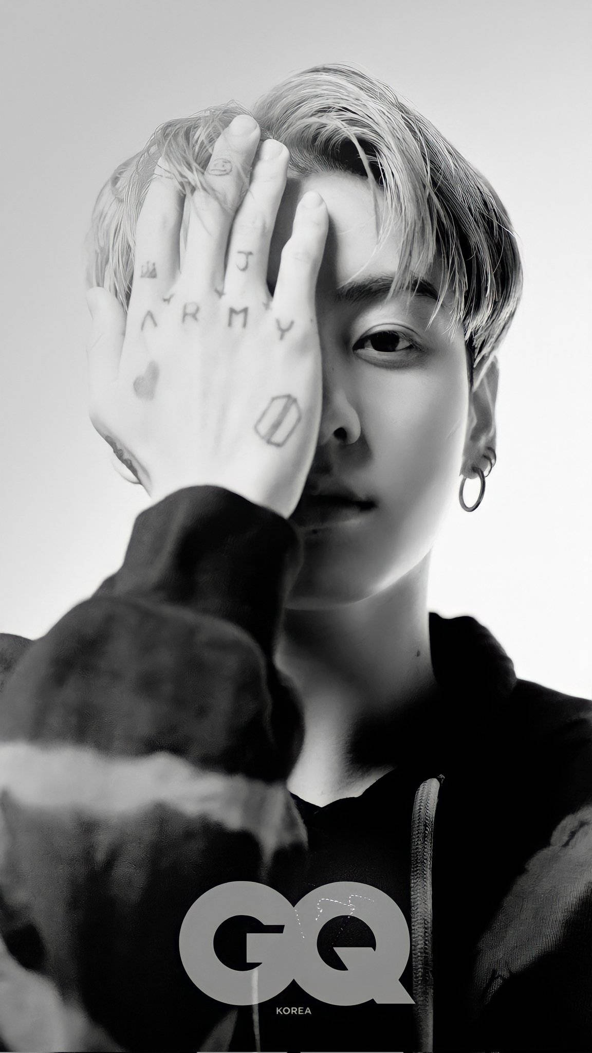 BTS JK黑白攝影 壁紙 — 一個年輕男子的黑白肖像，手部紋身遮蓋半邊臉，身穿連帽衫和圓環耳環。