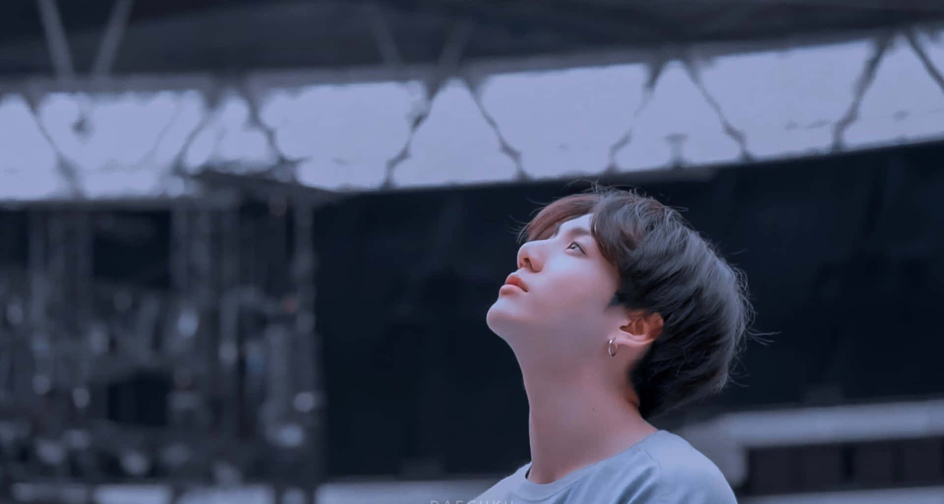 BTS Jungkook在頒獎典禮上演唱 壁紙 — 一位短黑髮的年輕男子在裂開的混凝土天花下，以冷藍色調露出平靜的表情向上凝視。