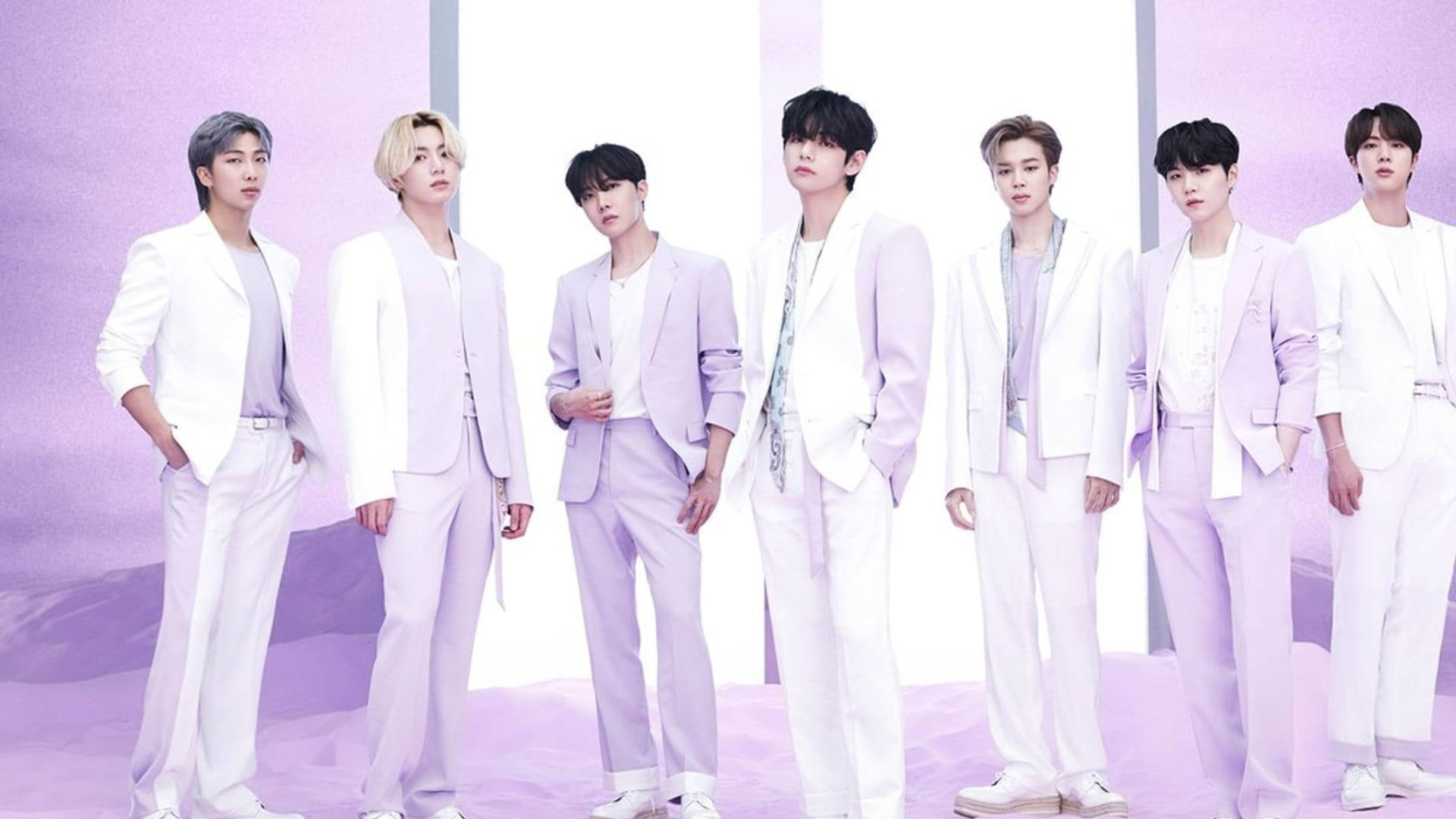 七位身穿白色和薰衣草色西裝的男士在紫色背景的攝影棚中擺姿勢。