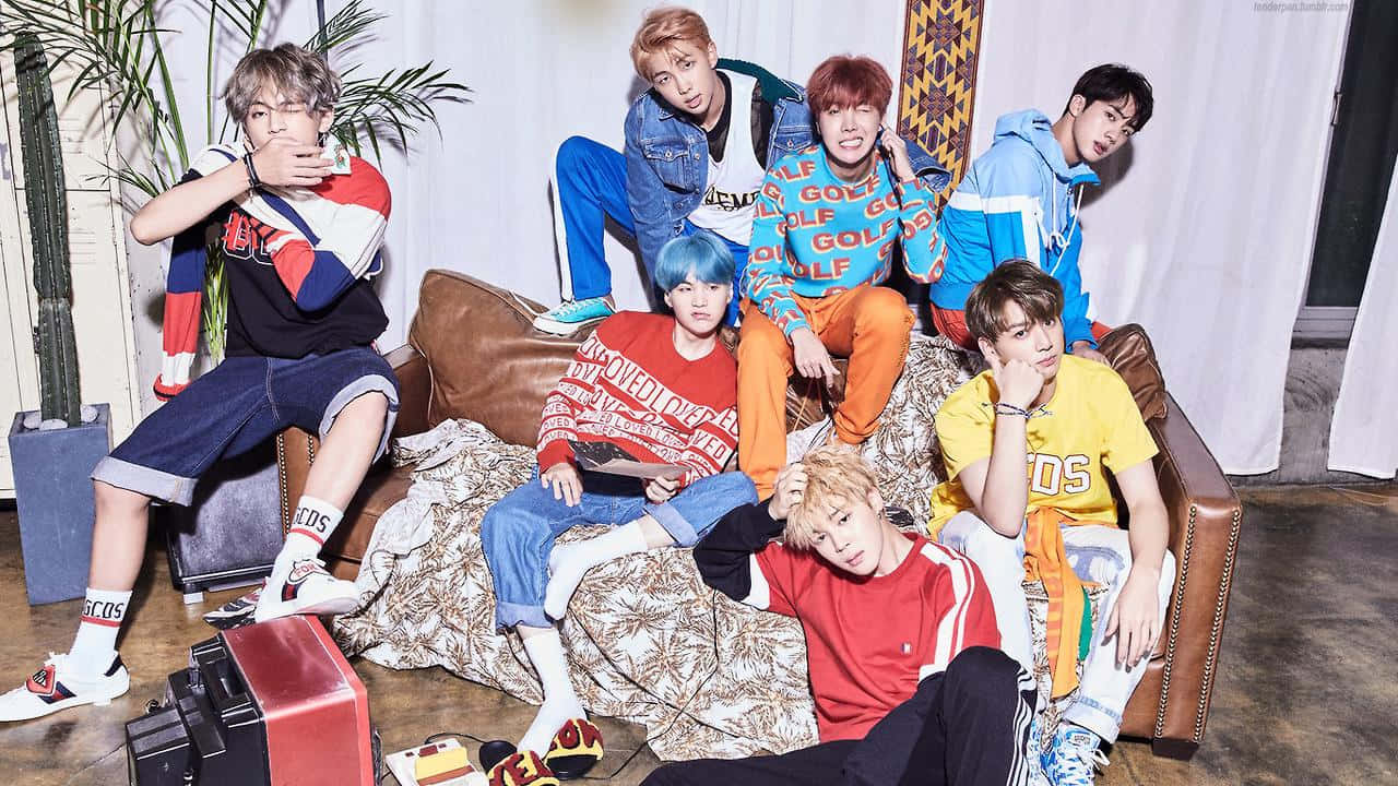 BTS MAC：時尚科技筆電，效能與美觀兼具 壁紙 — 七位時尚年輕男子身穿色彩繽紛的街頭服飾，在現代室內環境中隨意地坐在棕色皮梳化上擺姿勢。