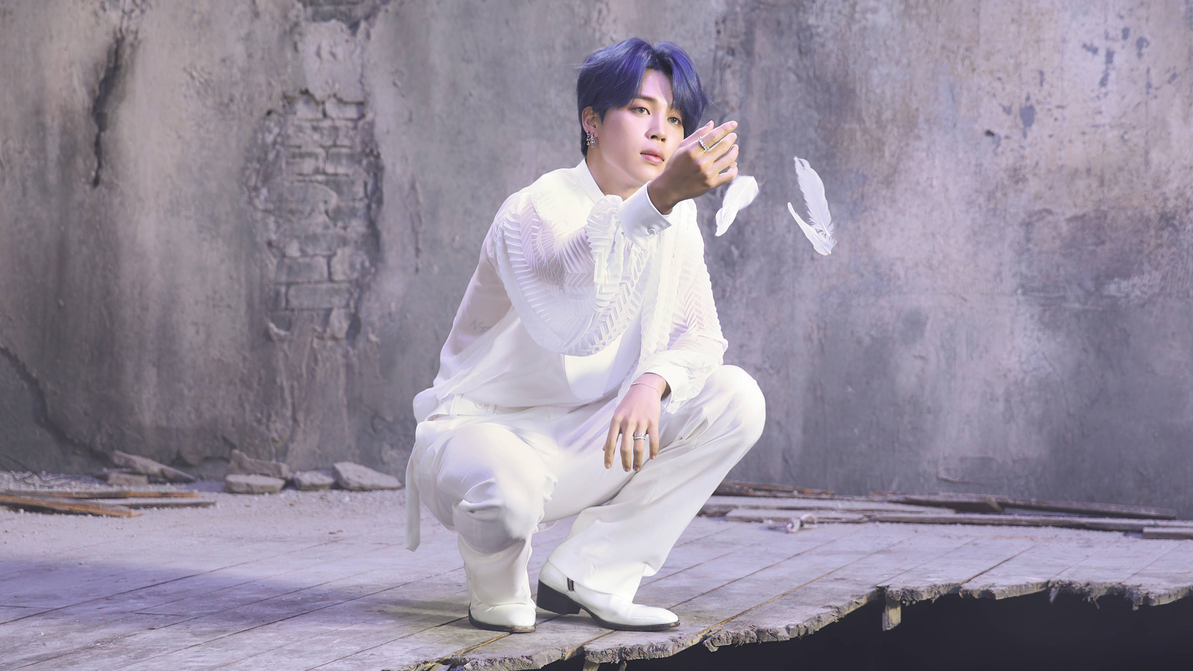 BTS 金珍洙《Map Of The Soul: 7》版本1 白鵝造型 壁紙 — 一位藍髮年輕男子身穿白色服裝，蹲在風化的木頭上，背景是裂開的混凝土牆，手持一根白色羽毛。