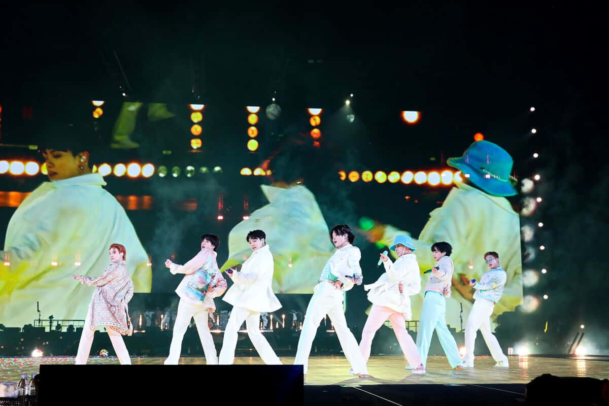 BTS《Permission to Dance》演出照 壁紙 — 穿著白色服裝的表演者在明亮的舞台燈光下跳舞，背景投影色彩繽紛。