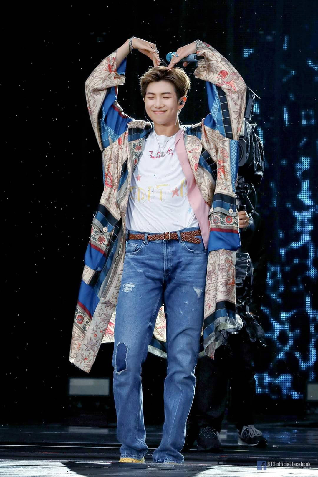 K-pop表演者在舞台上穿著圖案外套和牛仔褲做出心形手勢。