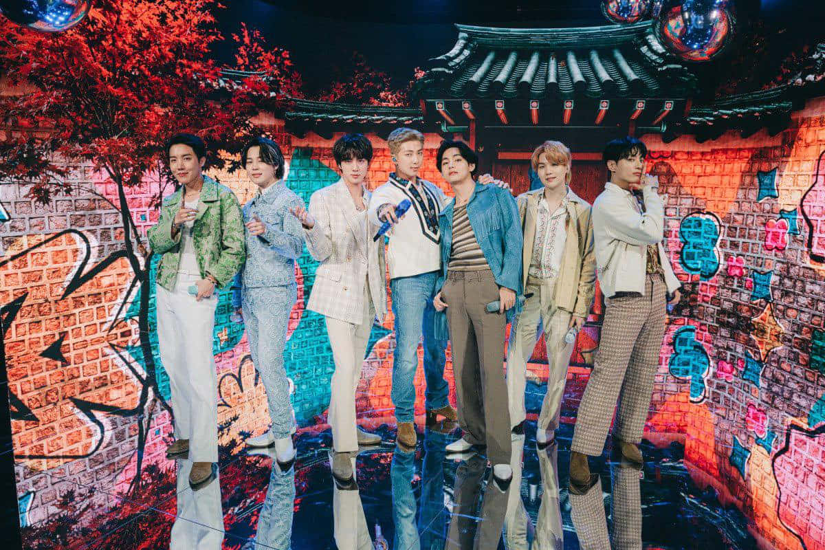 BTS《The Late Late Show with James Corden》節目照 壁紙 — 七位時尚男士在反射舞台上自信擺姿勢，背景是充滿活力的塗鴉牆和傳統韓國屋頂。