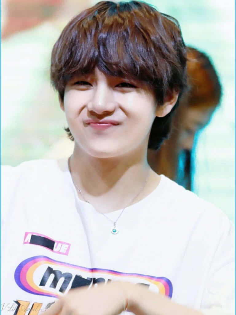 BTS V 展現自信笑容 壁紙 — 一位棕色頭髮的年輕男子穿著白色圖案T恤和項鍊，露出溫暖的笑容。