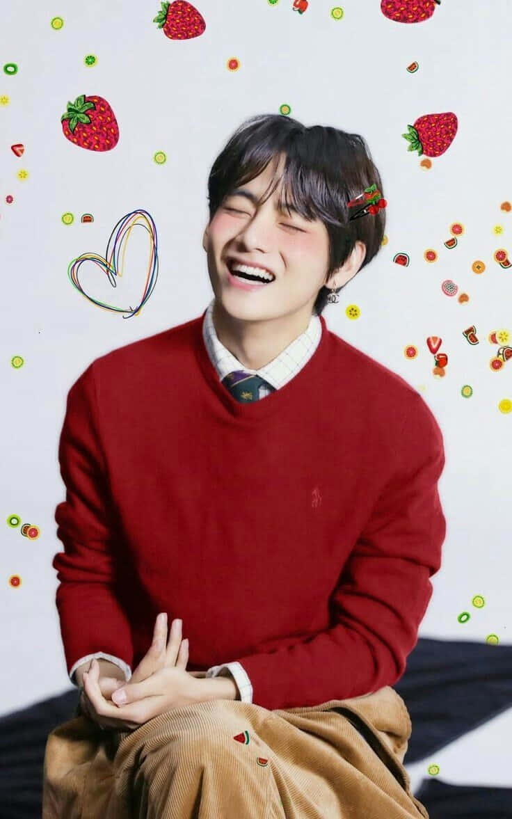 BTS V 展現致命魅力 壁紙 — 一個快樂的年輕男子穿著紅色毛衣，閉著眼睛在充滿草莓和彩色塗鴉的俏皮背景中大笑。