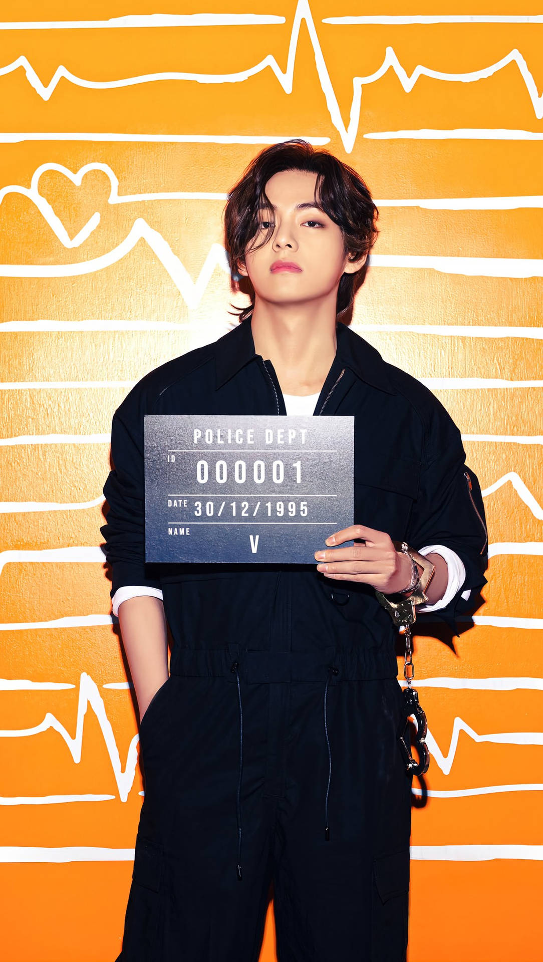 BTS V 持「通緝令」板照 壁紙 — 一名身穿黑色連身衣的年輕男子，在帶有白色心跳和心形線條圖案的鮮橙色牆壁前，手持帶有手銬的警察登記牌。