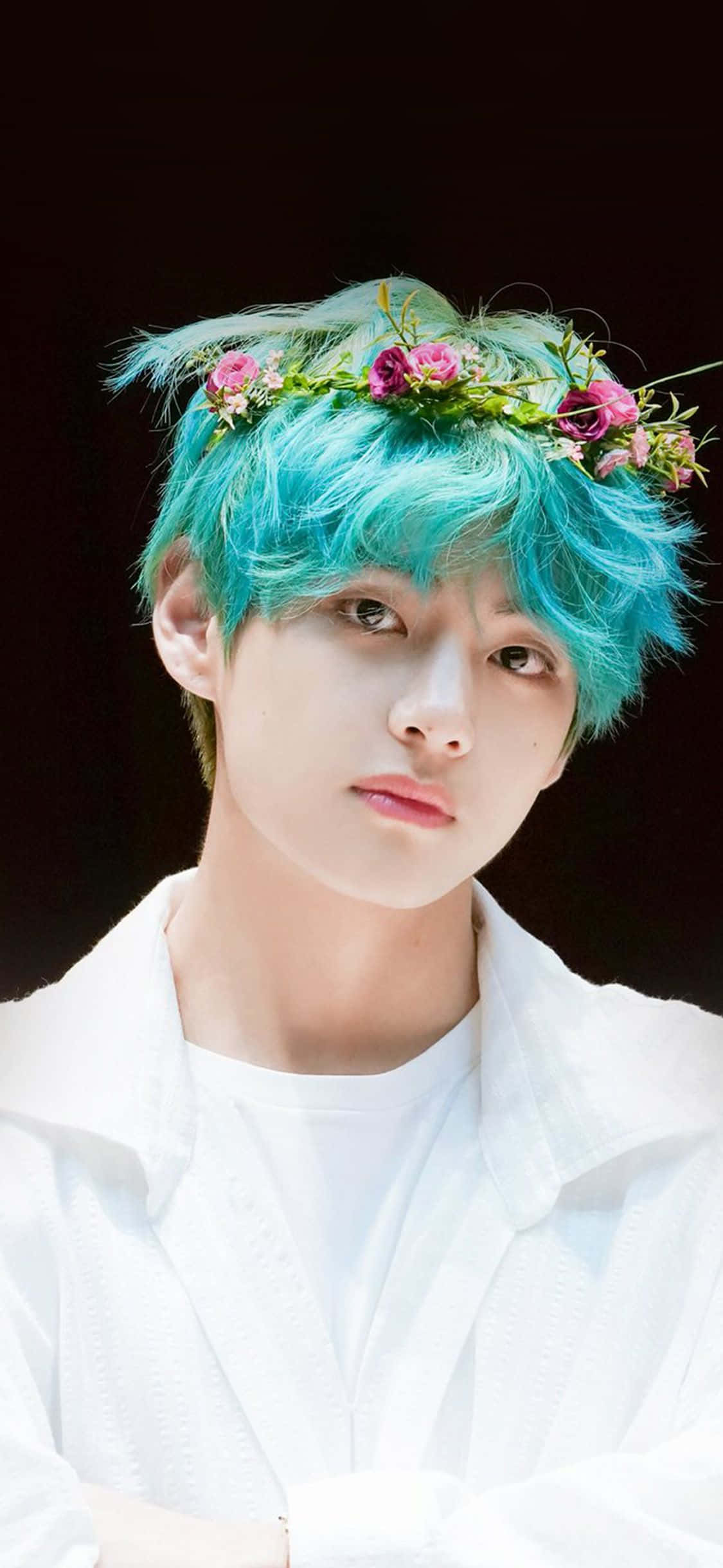 BTS V 散發青春喜悅與自信 壁紙 — 一位年輕男子擁有充滿活力的藍綠色頭髮，飾以粉紅色花冠，在深色背景下溫柔地凝視。