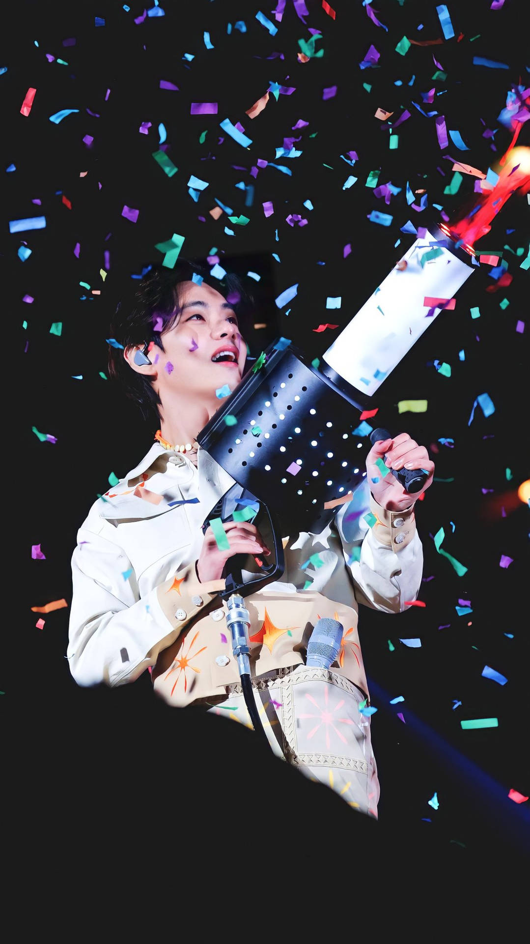 BTS V 派對煙花炮 壁紙 — 表演者愉快地從大炮中射出五彩紙屑，背景是黑暗的舞台。