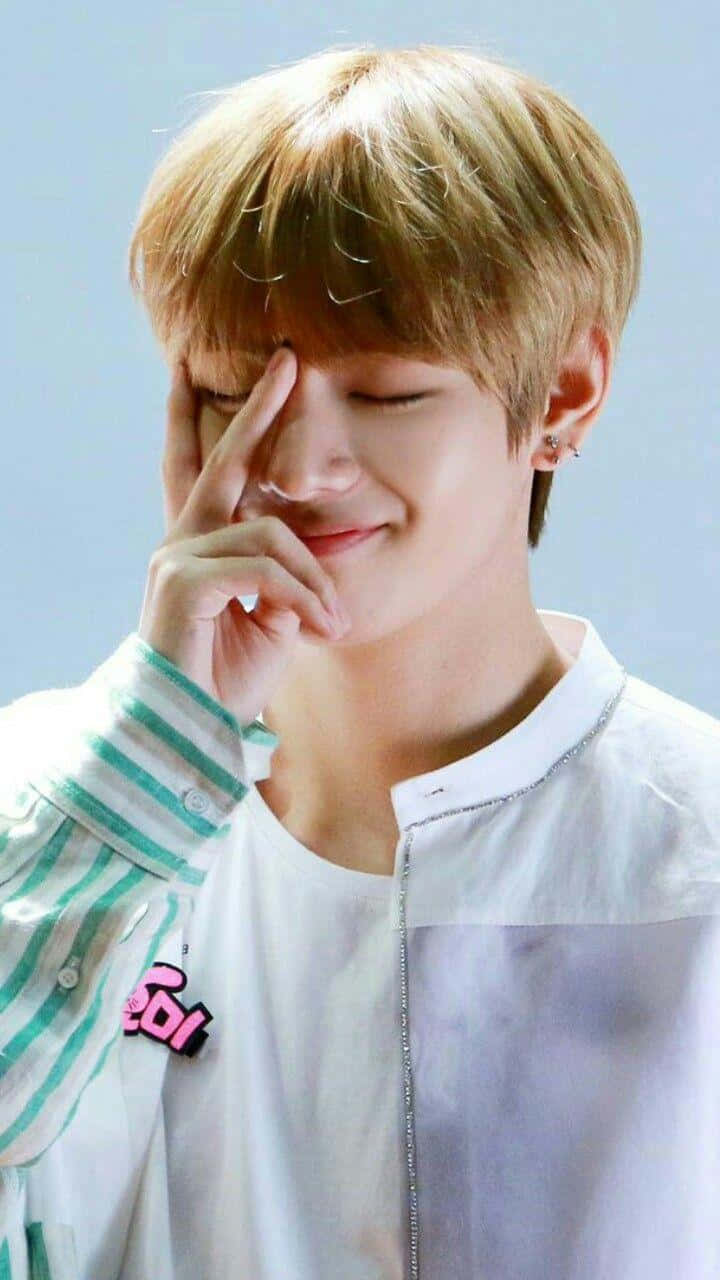 BTS V 為勝利而站 壁紙 — 一位金髮年輕男子在明亮的攝影棚中輕柔地觸碰眼睛，露出溫柔的微笑。