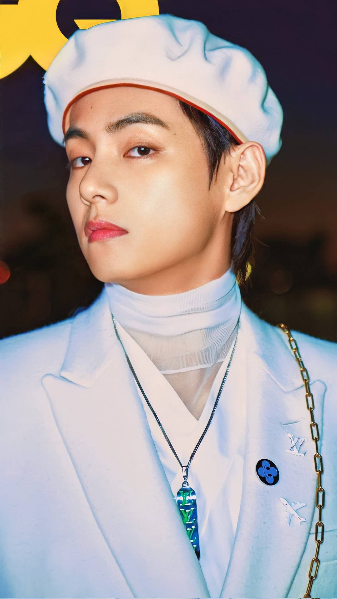 BTS V 白色貝雷帽造型 壁紙 — 一位戴著白色貝雷帽和訂製外套的年輕男子，在黑暗模糊的背景中，伴隨著溫暖的散景燈光，若有所思地凝視著。