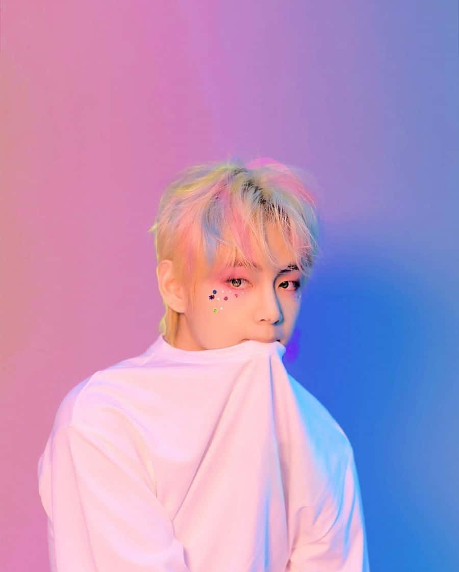 BTS V 的迷人肖像 壁紙 — 一位擁有柔和色調頭髮和彩色面部閃粉的人，在粉紅與藍色漸變的攝影棚背景前擺姿勢。