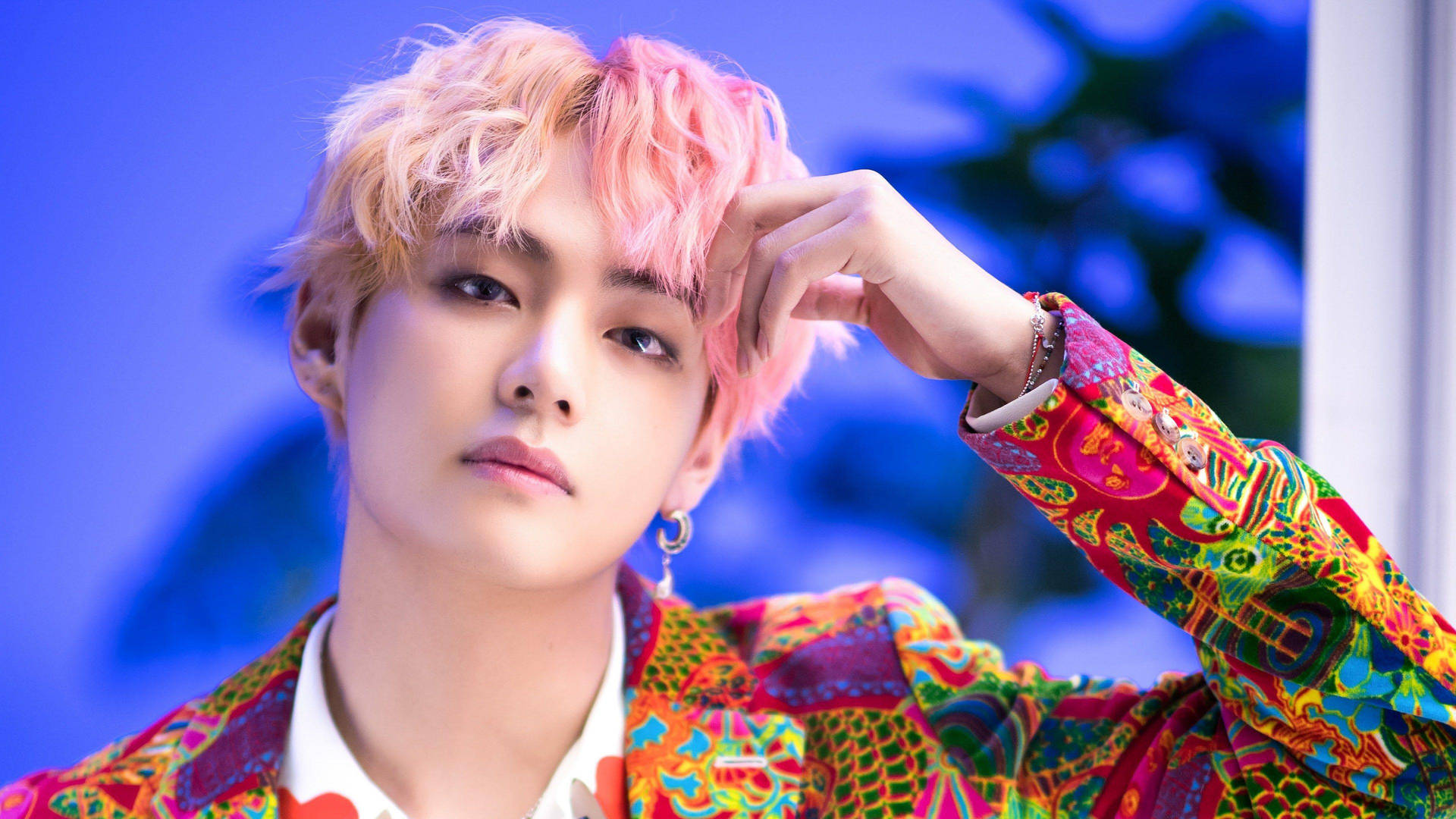 BTS V 色彩繽紛西裝 壁紙 — 一位粉紅頭髮、身穿彩色圖案外套的年輕男子在藍色背景前擺姿勢。