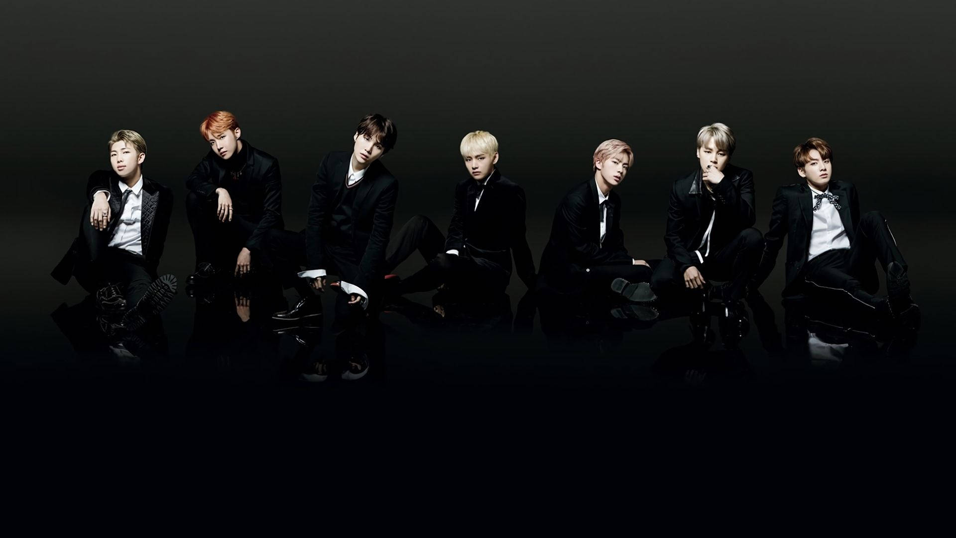 BTS黑色背景集體美學照 壁紙 — 七位穿著黑色西裝的時尚男士在黑色反光地板上自信地擺姿勢，背景為深色。