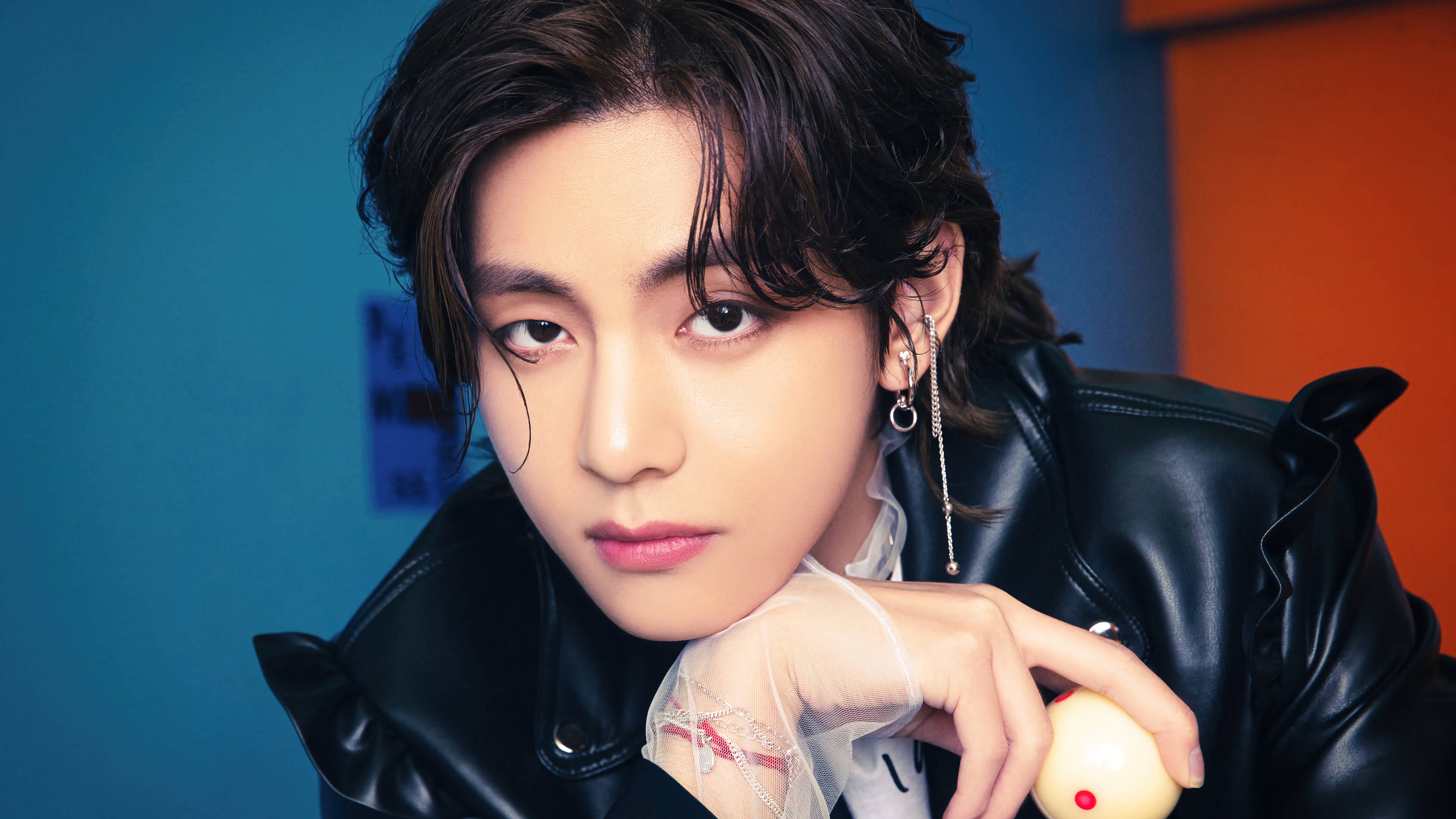 BTS 田柾國皮夾克 壁紙 — 一位黑髮、眼神銳利的年輕男子身穿黑色皮褸，在藍色和橙色背景前手持一個黃色小物件。