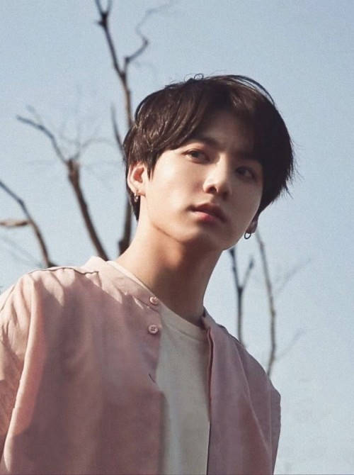 BTS 可愛美學 崔勝哲 壁紙 — 一位深色頭髮、戴著耳環的年輕男子，在淡藍色天空和光禿樹枝的背景下，若有所思地向上凝視。