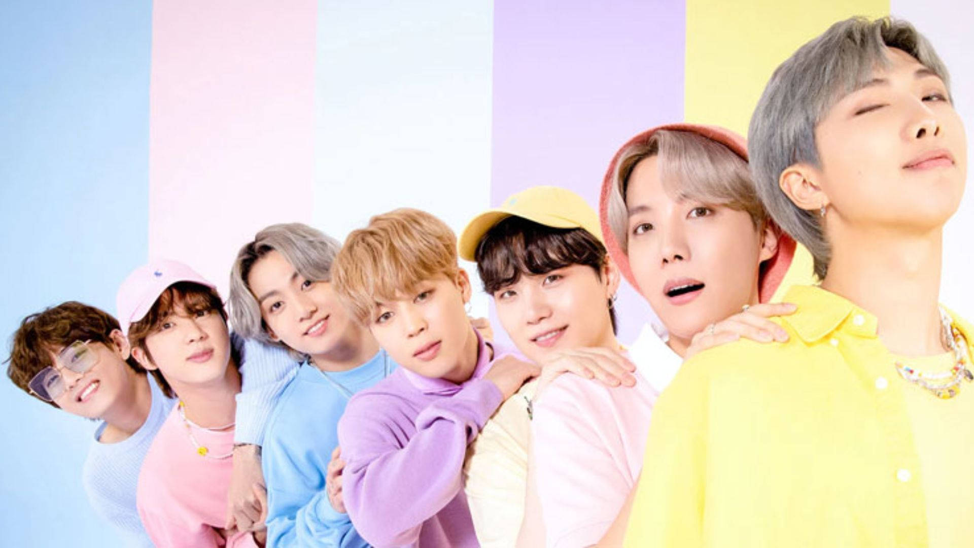 BTS 可愛風格：柔和色系服裝與背景 壁紙 — 七位身穿柔和色調服裝的年輕男性在充滿活力的條紋背景前緊密擺姿勢。