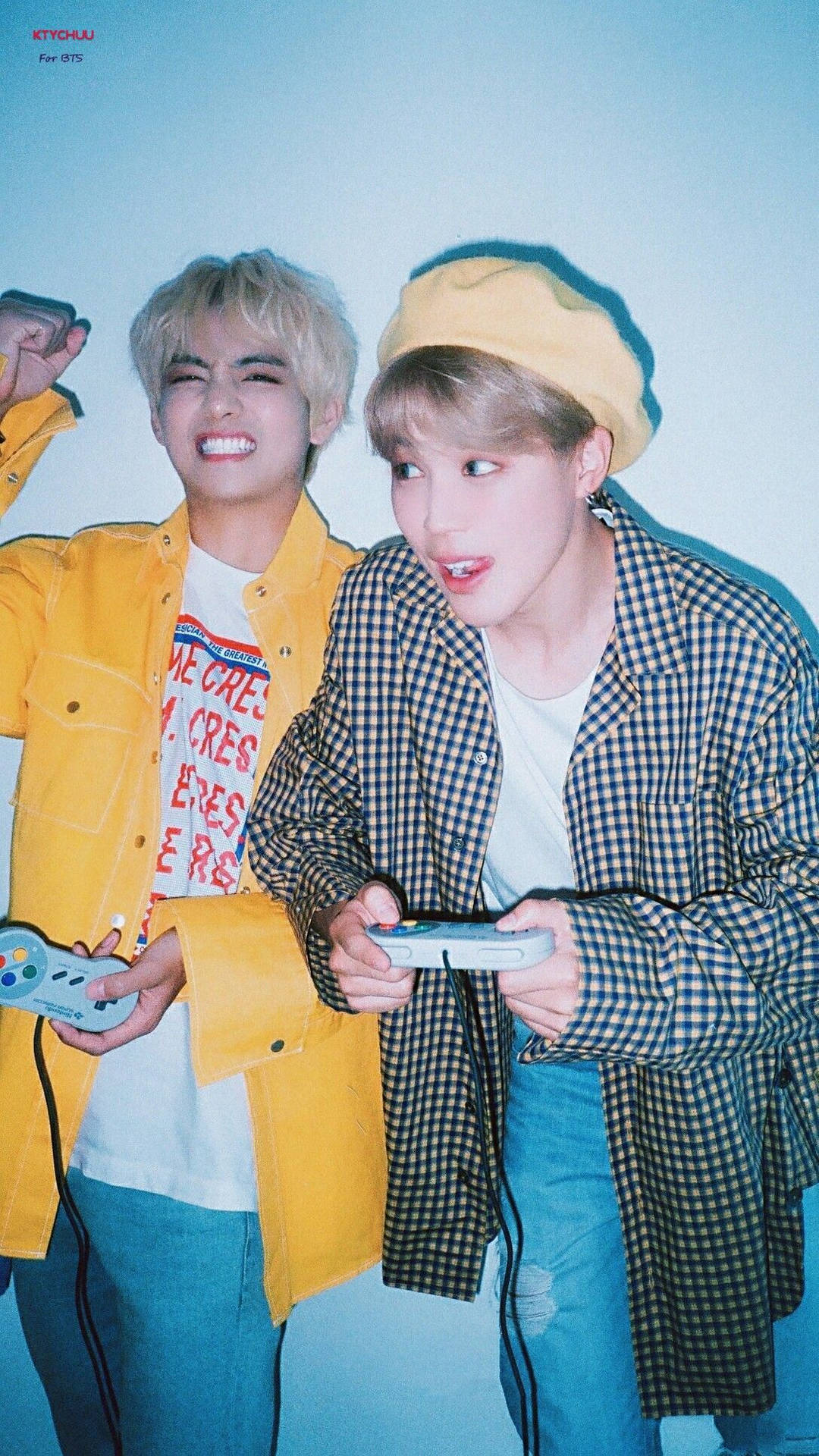 BTS 吉米與 V 2020 壁紙 — 兩名身穿鮮豔黃色和格仔服裝的年輕男子，在酷炫的藍色背景下，熱情地使用控制器玩復古電子遊戲。