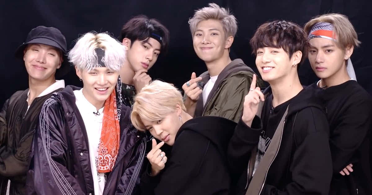 BTS 在《艾倫秀》的可愛合照 壁紙 — 七位時尚年輕男子，擁有色彩繽紛的頭髮和潮流服飾，在黑色背景下自信地擺姿勢。