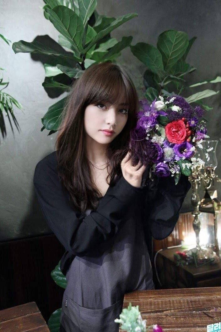 女性在室內靠近綠色植物手持彩色花束。