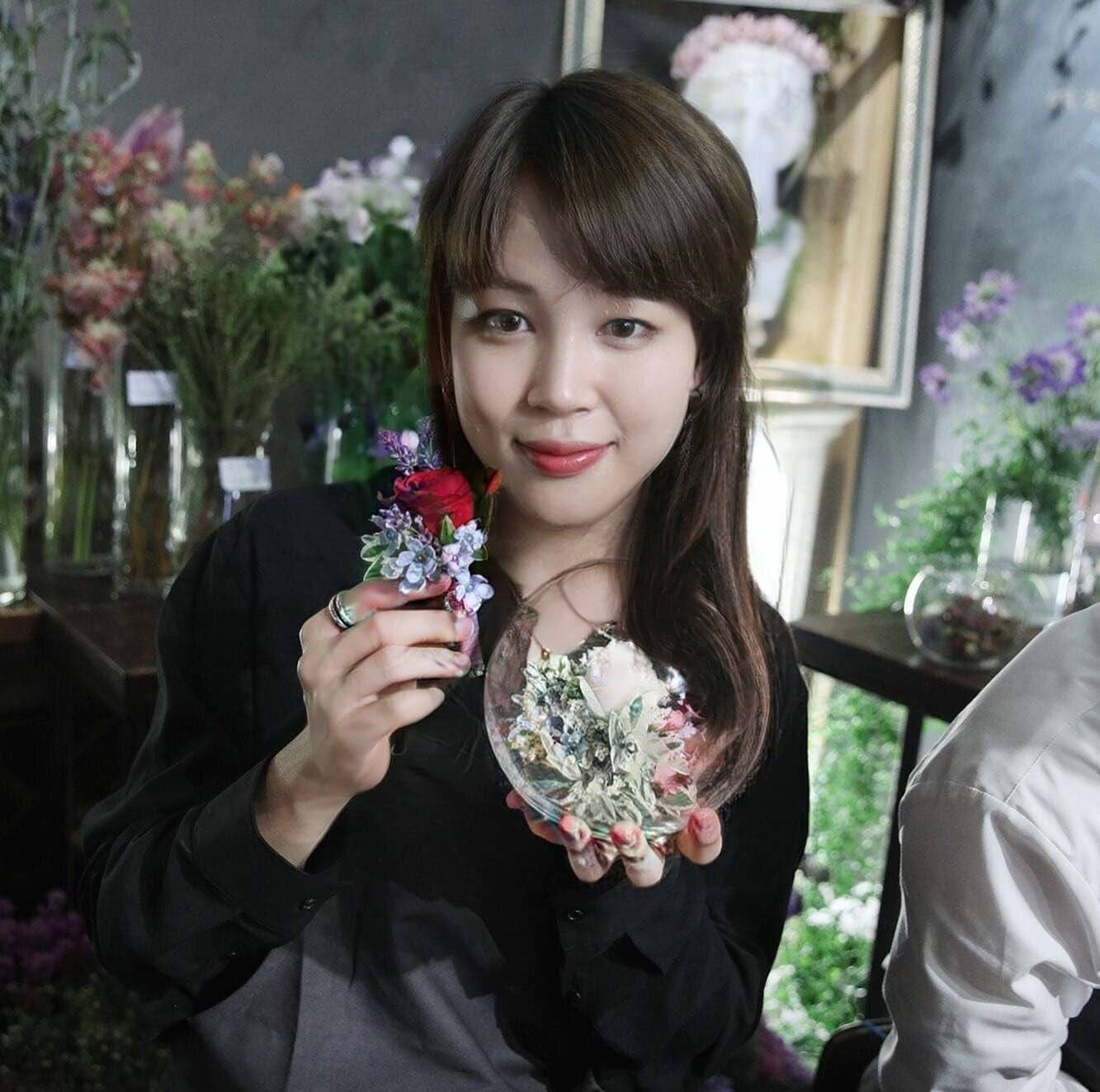 女性在花店裡手持花卉佈置和裝有保鮮花的玻璃罩。