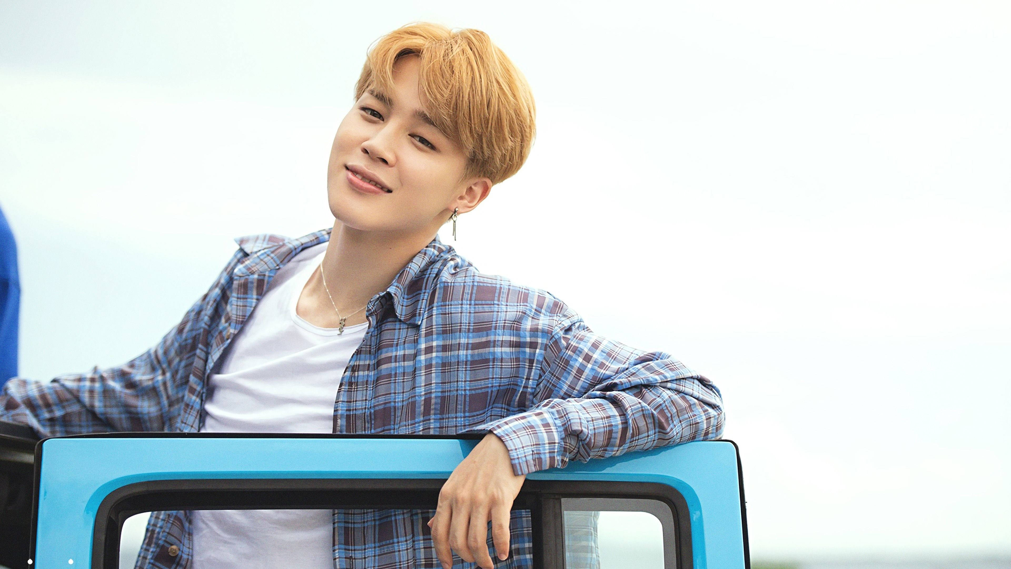 BTS 崔勝哲 可愛凝視 壁紙 — 一位橙髮年輕男子隨意靠在一輛亮藍色車門上，在蒼白的天空下溫柔微笑。