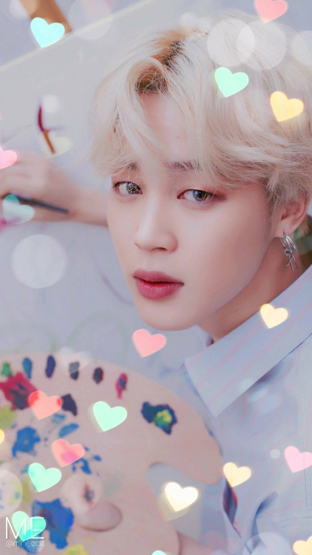 BTS 崔勝哲 可愛心形 壁紙 — 一位金髮年輕男子手持調色板，溫柔地凝視著，發光的愛心在夢幻的粉彩薄霧中漂浮在他周圍。